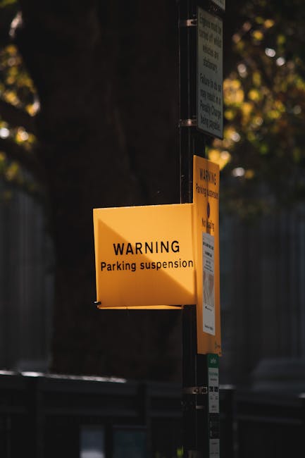 A yellow rectangular warning sign attached to a metal pole displaying the message 'WARNING Parking suspension' in black text. The sign is located outdoors in a residential area, with blurred backgroun